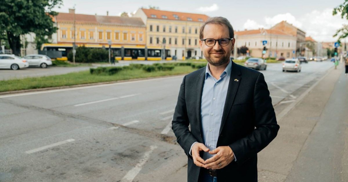 Dominic Fritz, îmbrăcat într-un sacou negru, pantaloni negri și o cămașă bleu, stând cu mâinile împreunate în fața abdomenului, zâmbind, în Piața Mocioni din carierul Iosefin, Timișoara, august 2025