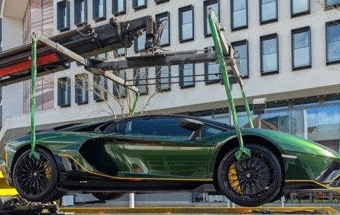 Lamborghini Aventador verde ridicat de o macara cu chingi speciale în fața unei clădiri