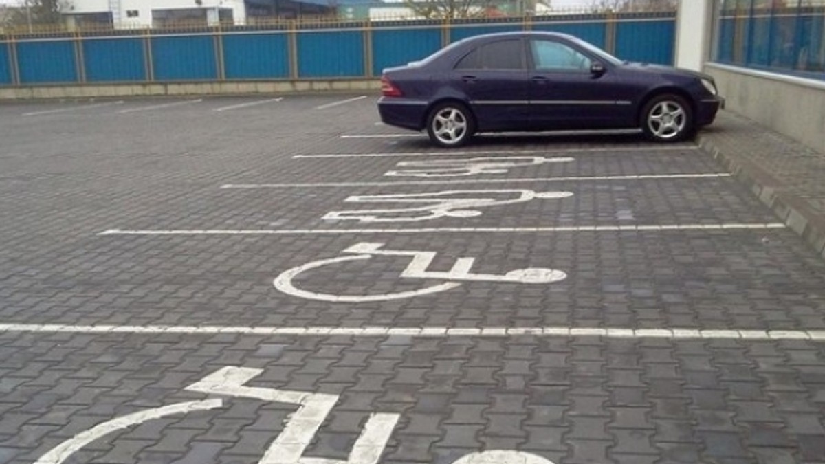 maşină pentru persoanele cu dizabilităţi, controlată prin telefonul mobil. Locuri de parcare destinate persoanelor cu dizabilități fizice. În plan îndepărtat, un Mercedes (de culoare închisă) parcat