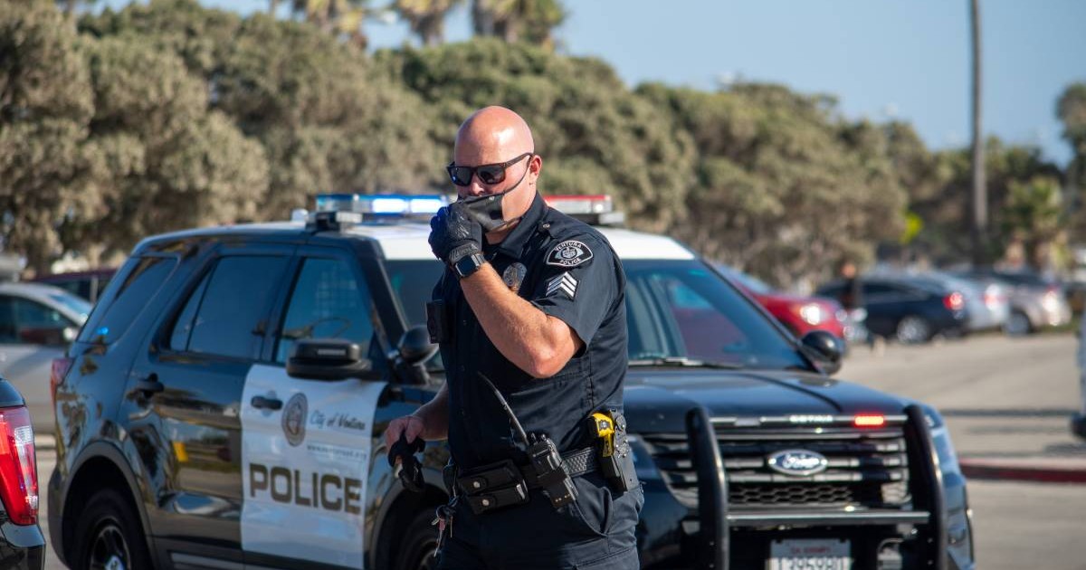 Un polițist din California, în uniformă, în timpul unei intervenții. Bărbatul stă în mașinii de Poliție