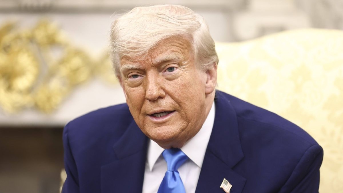 Imagine prim plan cu Donald Trump, un sacou inchis la culoare si cravata breu, cu o insigna in piept, in biroul oval, cu fundal alb-auriu