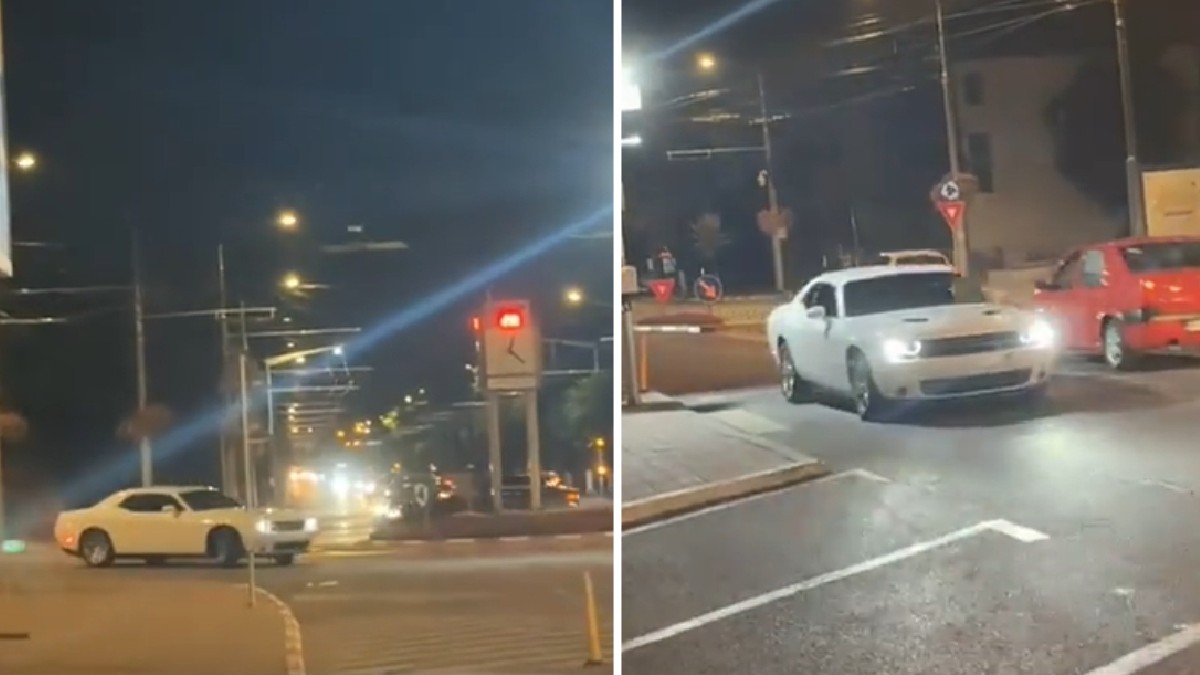 O mașină albă sport este surprinsă circulând noaptea printr-o intersecție iluminată.