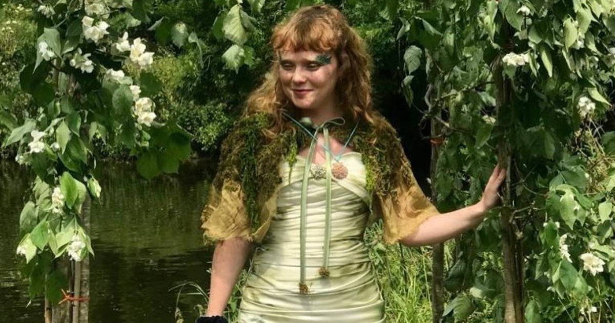 Tânăra Meg Avon, intr-un cadru de ceremonie, intre plante verzi, cu o roche vernil si o pelerina din muschi