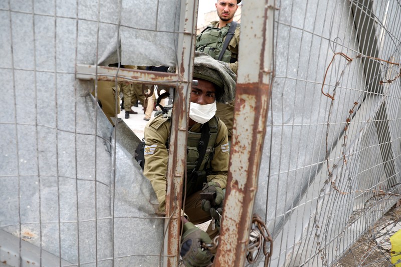 Un soldat israelian, cu masca de rigoare pe față, deschide porțile pentru turiștii care vor să viziteze vechiul oraș Hebron, pe 9 mai 2020. EPA-EFE/ABED AL HASHLAMOUN