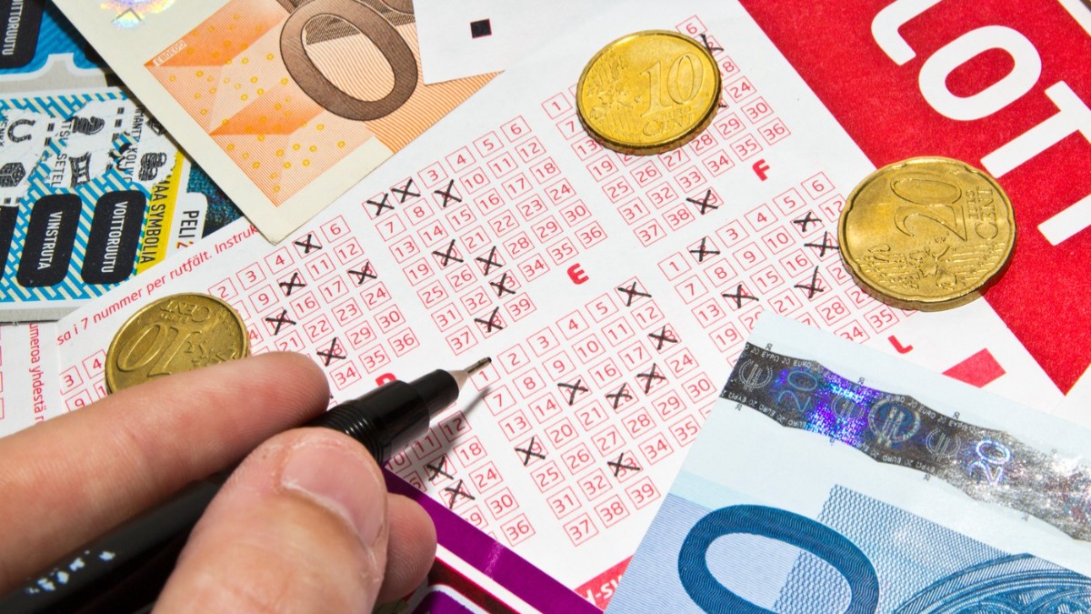 O persoană care bifează pe un bilet la loto. Pe acesta se află monede și bancnote euro.