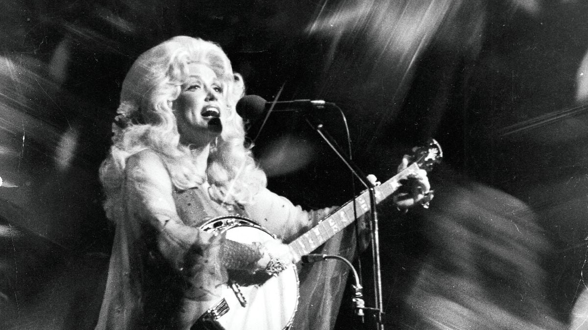 Dolly Parton, pe scenă, cu o chitară, în fața unui microfon