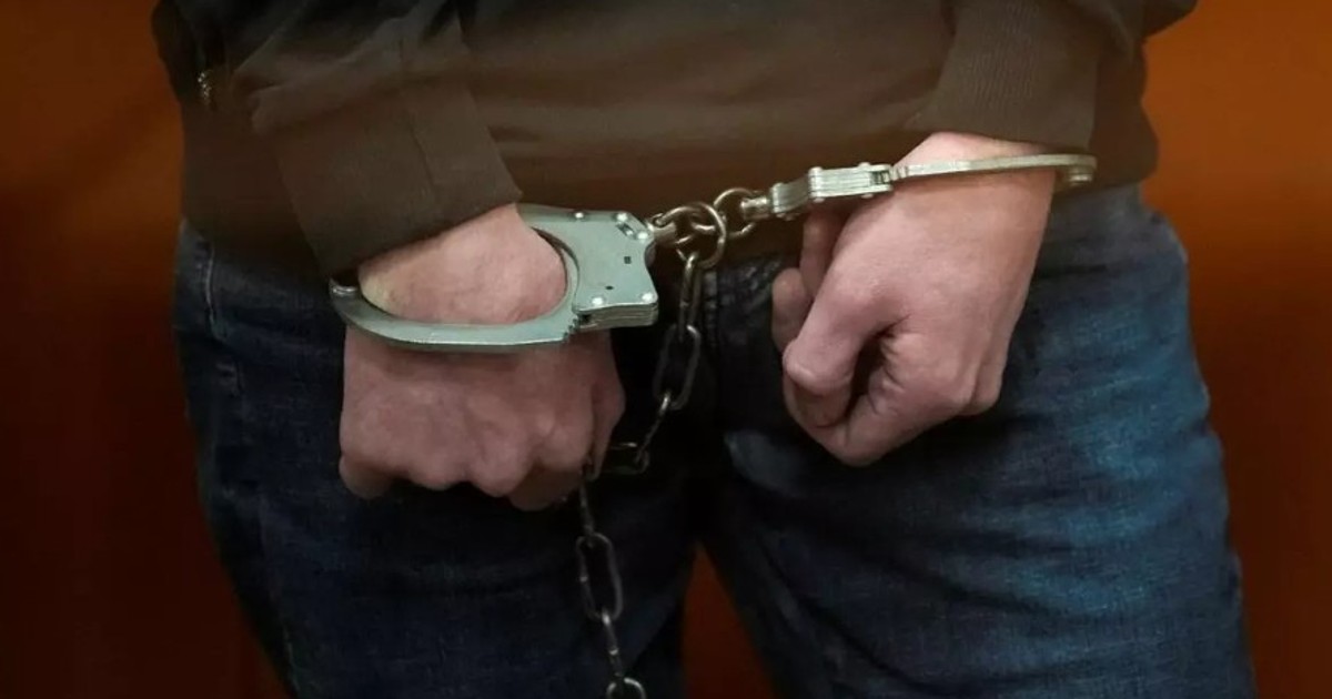 Bărbat arestat, cu cătușe la mâini. Suspectul poartă un pulover și o pereche de blugi