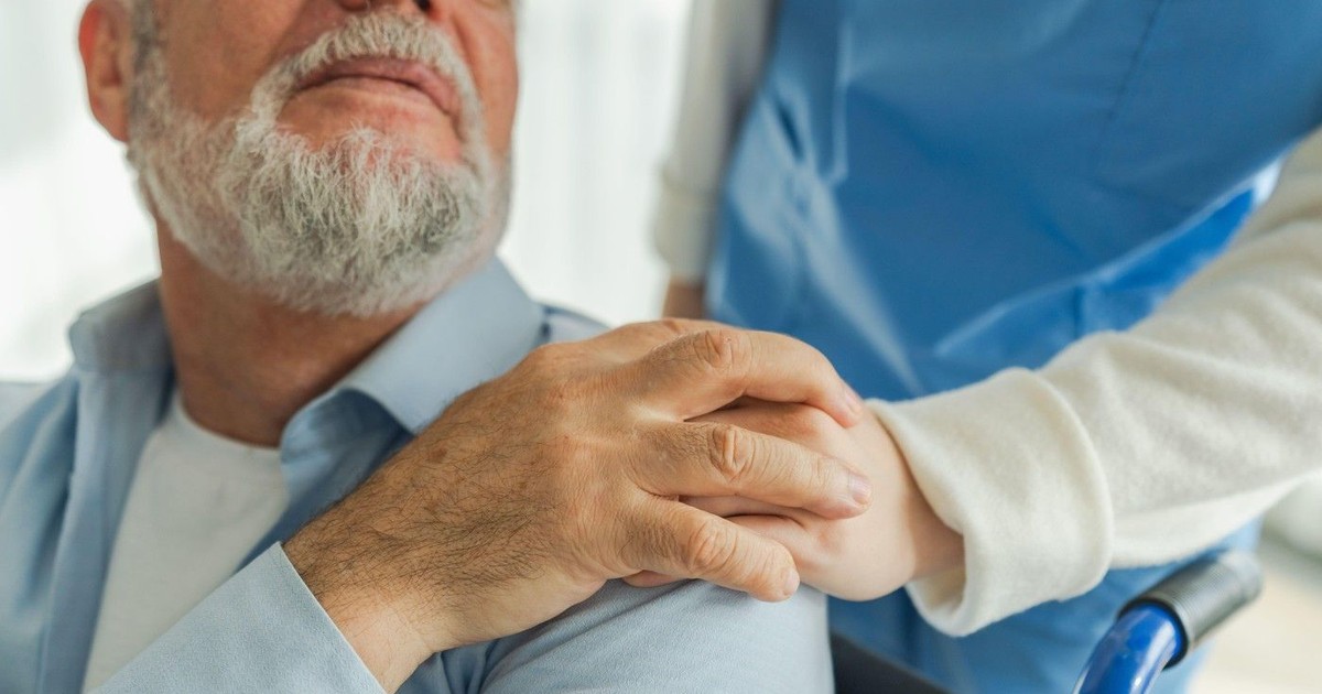 Asistentă medicală care ajută un bătrân în scaun cu rotile.