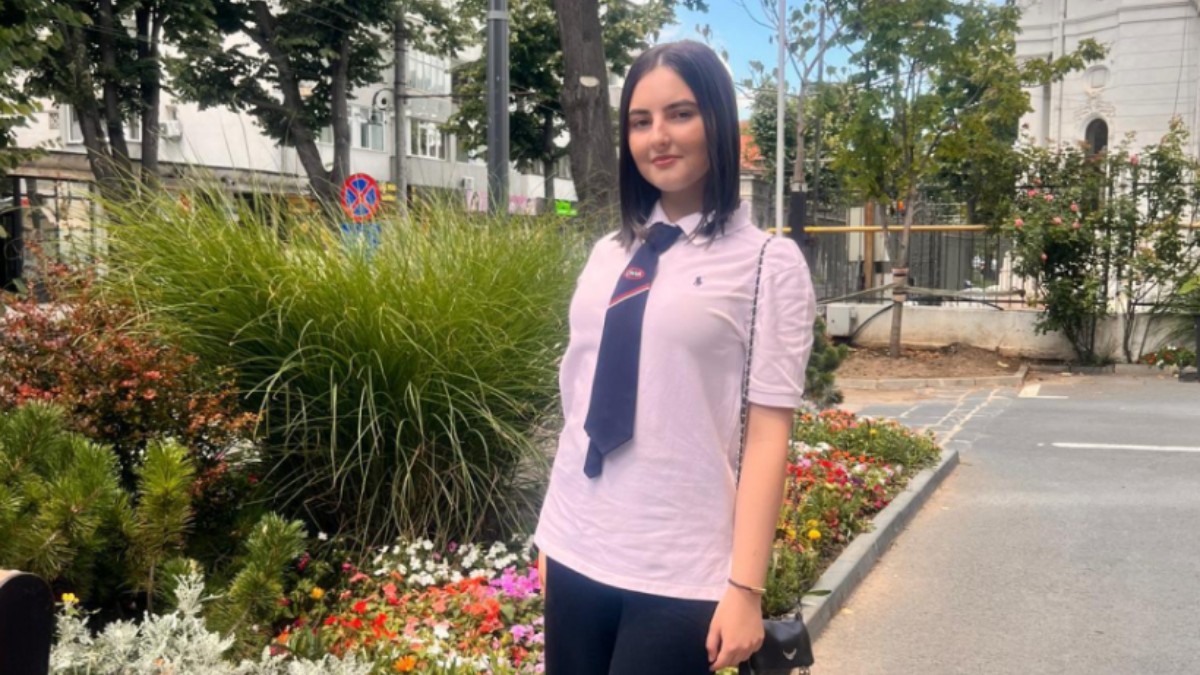 Bianca Aramă, îmbrăcată în tricou roz, cravată și pantaloni negri