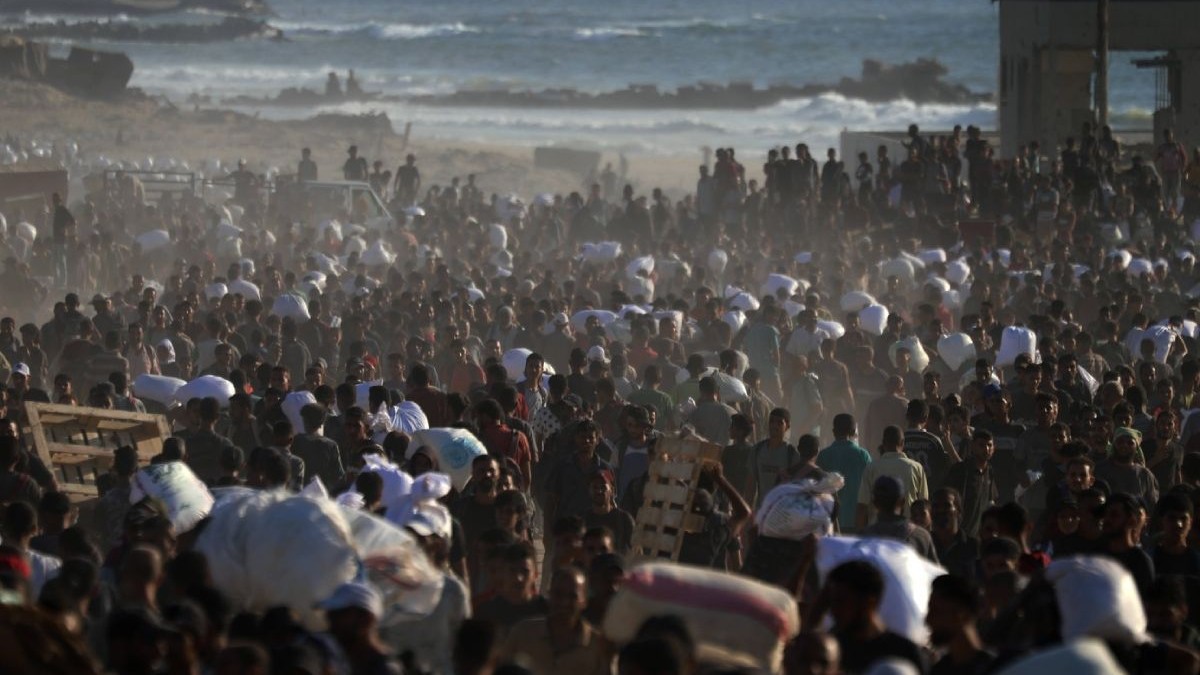 Palestinienii, aduși în pragul foametei din cauza atacurilor și blocadei armatei israeliene, se adună la o distribuire de ajutoare. mii de oameni se imbulzesc pentru mancare si cara saci in spate