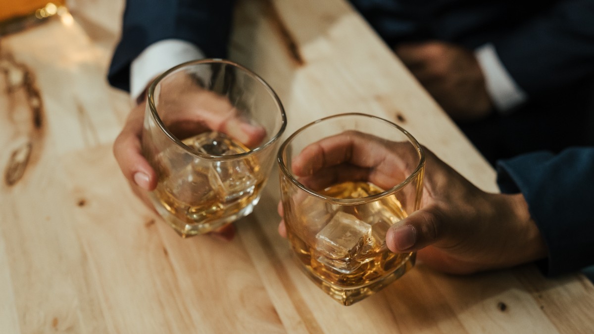 Doi bărbați în timp ce stau la masă și beau alcool într-un bar, sunt îmbrăcați la costum