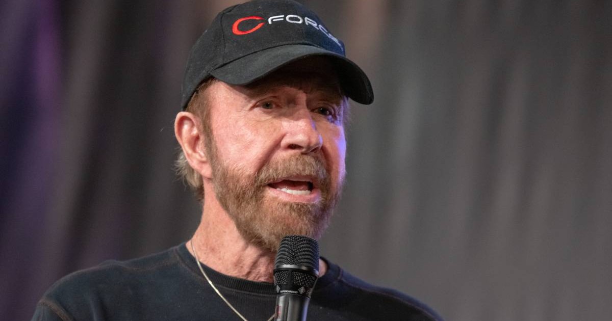Chuck Norris, cu sapca neagra și bluza neagra, vorbeste la microfon, 2018