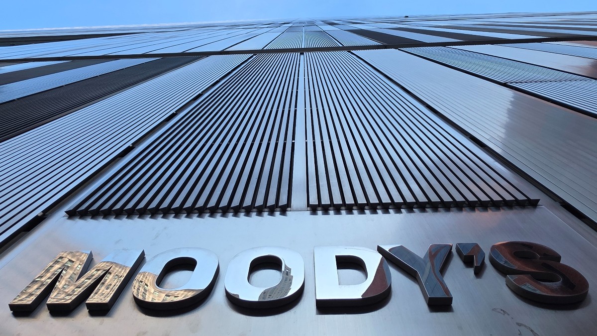 Imaginea prezintă o vedere alb-negru în perspectivă de jos în sus a fațadei unei clădiri moderne, pe care este inscripționat numele agenției Moody's.