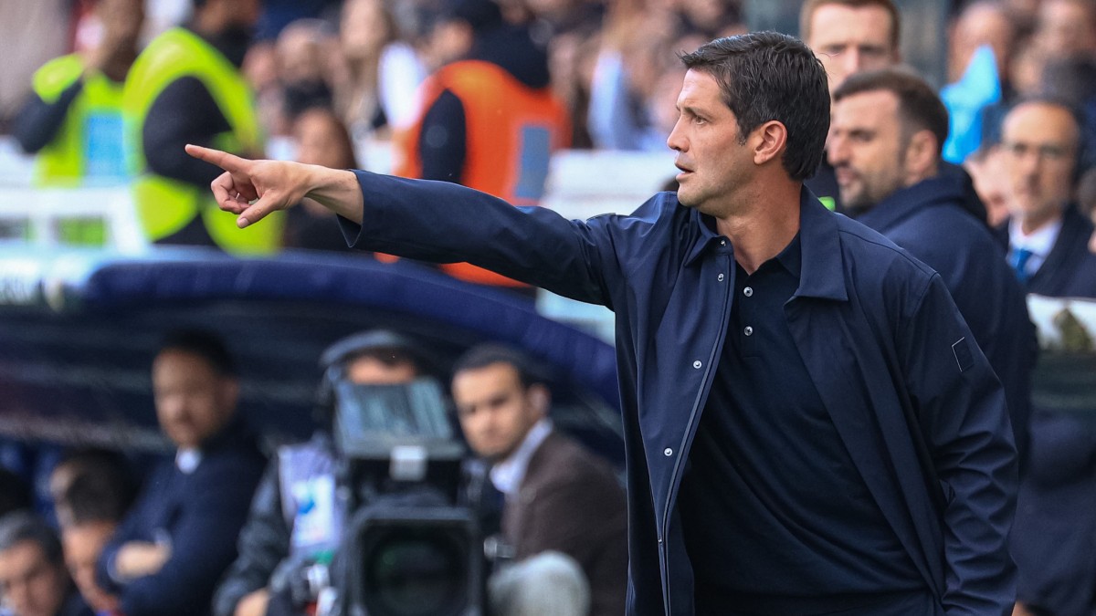 Cristi Chivu, într-o tribună din Parma, Italia, alături de mai mulți suporteri, în timpul unui meci de fotbal. Este îmbrăcat cu o bluză neagră, peste care are o cămașă desfăcută, bleumarin, și arată cu degetul spre teren.