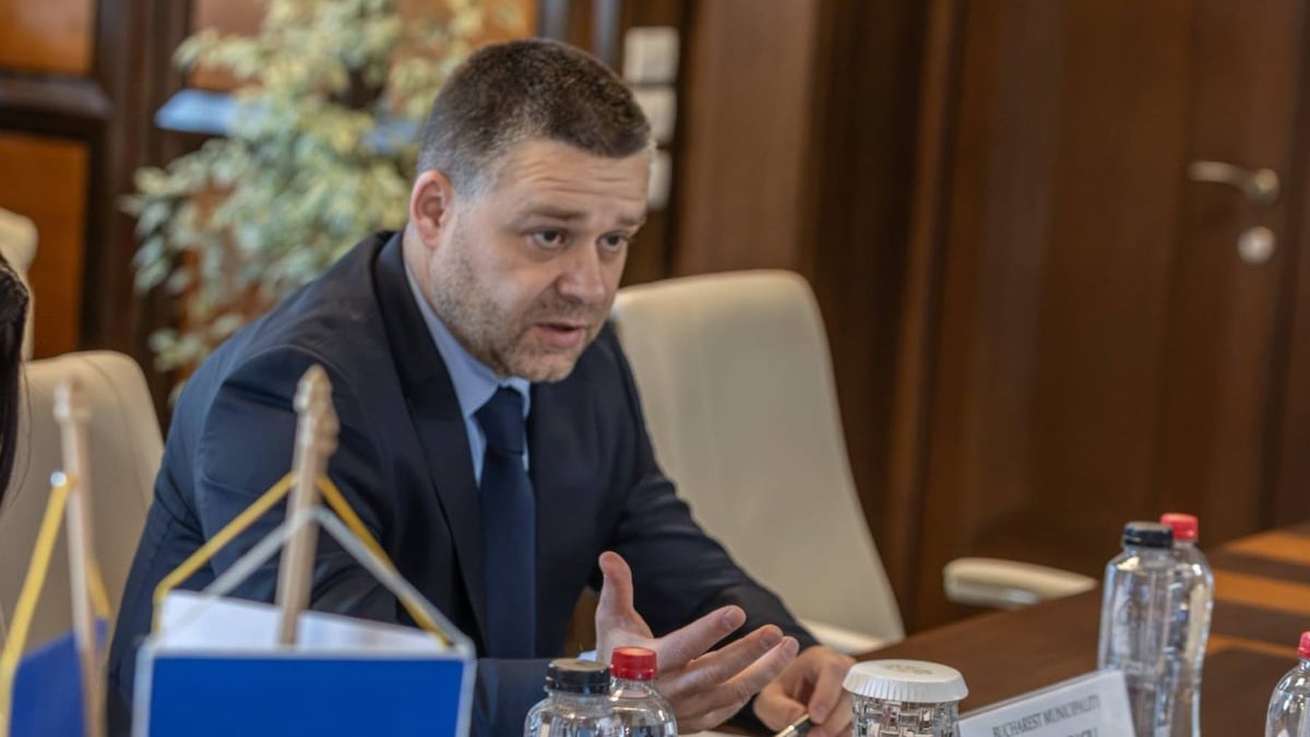 Primarul Capitalei, Ciprian Ciucu, în timp ce stă la birou într-o sală de ședințe, îmbrăcat la costum