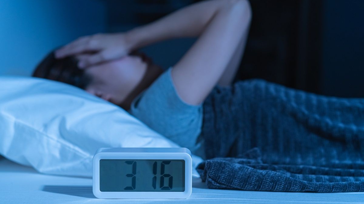 Tânără asiatică iritată, stresată, anxioasă, care suferă de insomnie, frustrată că stă trează în pat noaptea, cu dureri de cap sau migrene, cu probleme de sănătate, deranjată de zgomotul puternic, incapabilă să adoarmă.
