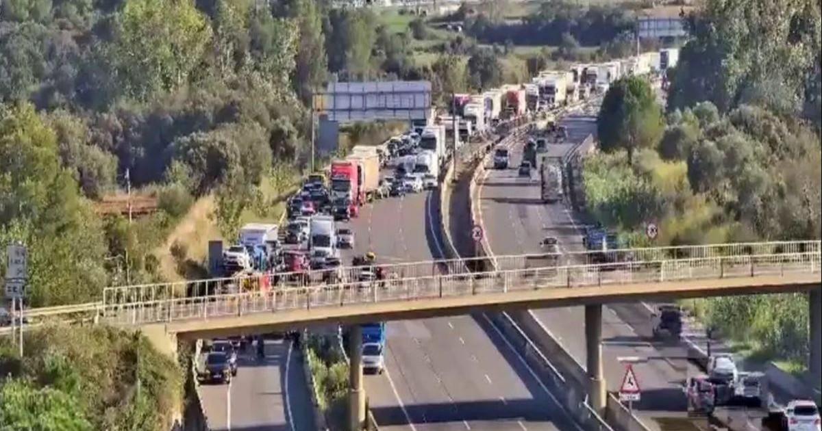 În prim-plan se vede o pasarelă, iar jos o autostradă cu mai multe sensuri de mers unde a avut loc un accident între două TIR-uri și s-a format o coloană de mașini în spate, în Spania, 19 septembrie 2025.