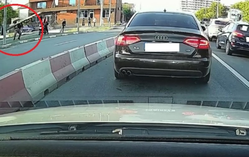 Un bărbat care a fost lovit în cap de un stâlp, pe trotuar. Pe șosea se observă mai multe mașini