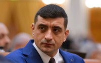 George Simion, îmbrăcat într-un costum albastru, cămașă albă și cravată neagră, în Parlament, pe fundal blurat, pe 26 aprilie 2026