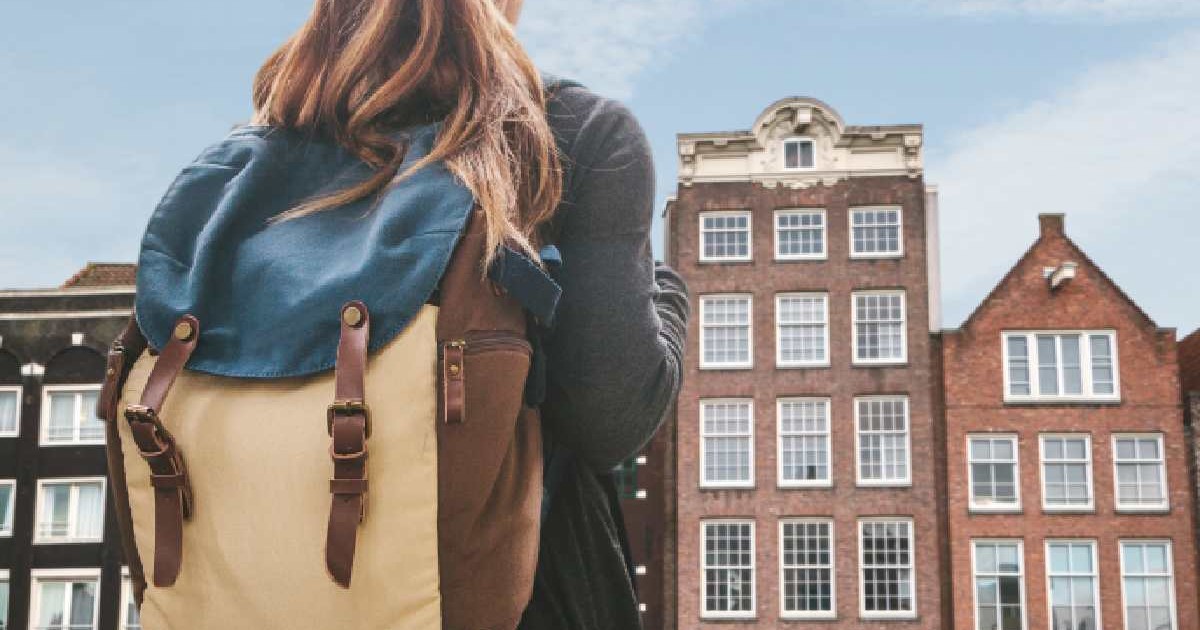 O tânără cu un rucsac se uită la casele tradiționale din Amsterdam, capitala oficială a Țărilor de Jos
