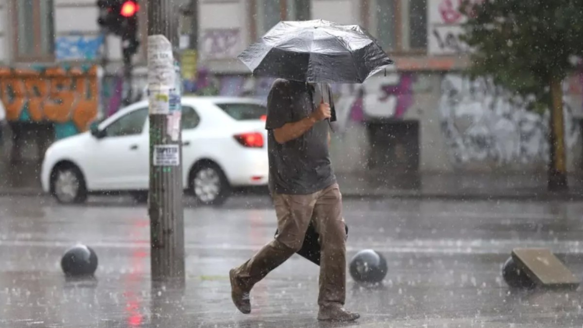 În imagine este ilustrat un bărbat care merge pe o stradă, în timp ce plouă. Acesta ține o umbrelă deasupra capului.