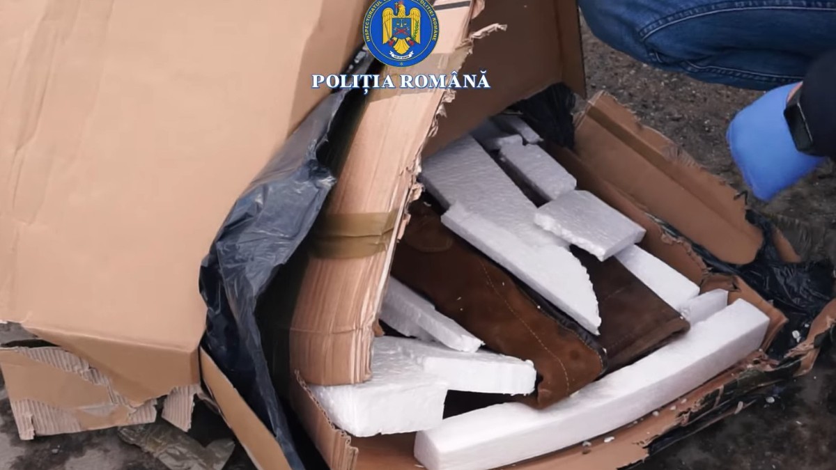 Un colet din carton desfăcut de polițiști în care se află o pereche de cizme maro, în care sunt ascunse arme