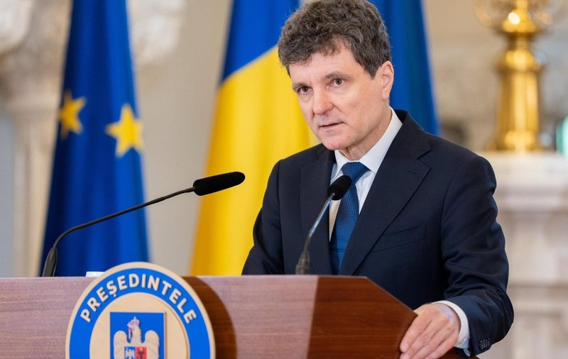Imaginea îl prezintă pe Nicușor Dan vorbind de la o tribună oficială, având în fundal steagurile României și Uniunii Europene.