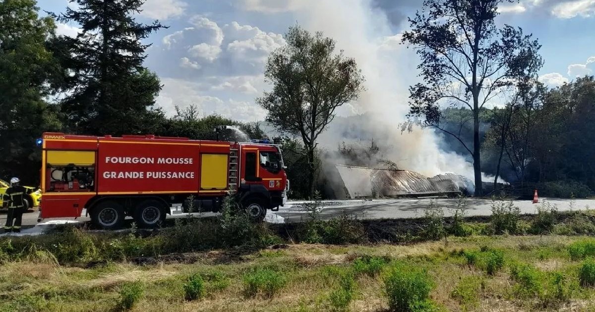 O mașină de pompieri pe șosea și un camion care arde, răsturnat în șanț