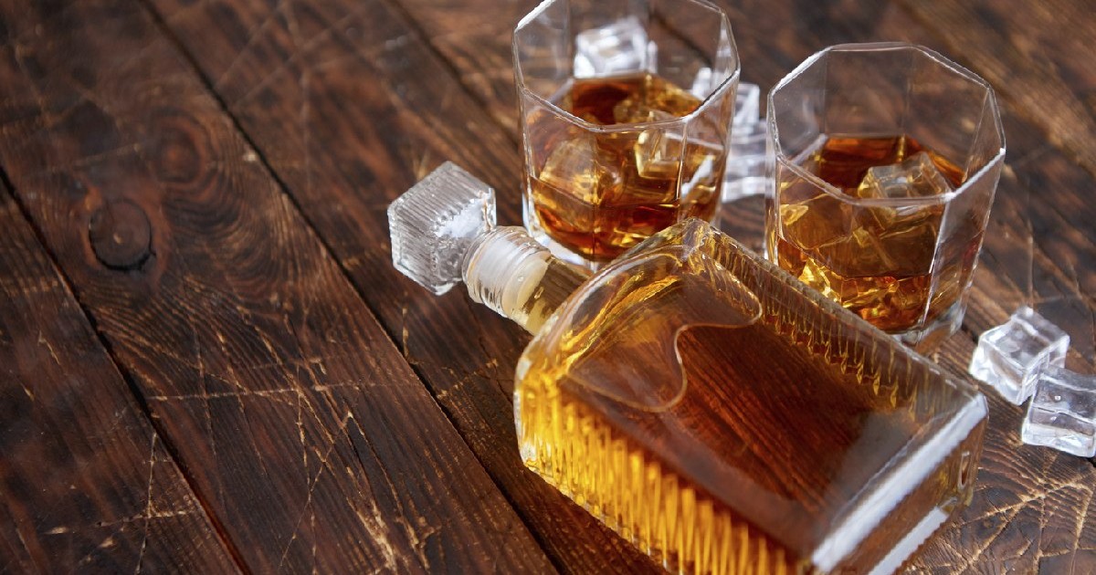 Sticlă de whisky cu două pahare așezate pe o masă rustică din lemn