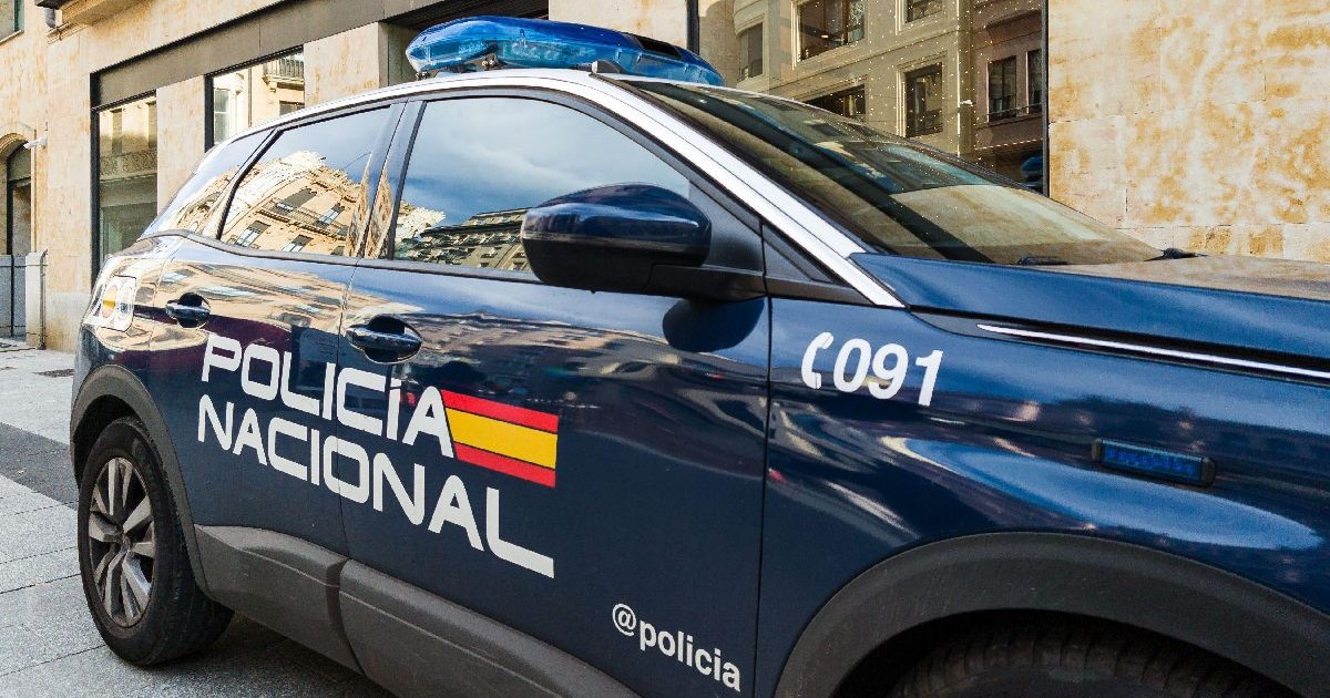 Fotografie cu un vehicul albastru al Poliției din Spania, cu o bară luminoasă albastră, parcat pe o stradă.