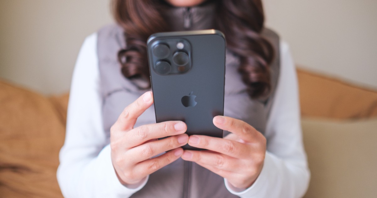 O femeie cu părul șaten, ține un iphone negru în mână și caută ceva pe telefon