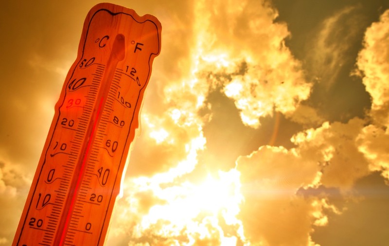Un termometru ce indică o valoare ridicată de aproximativ 36 de grade Celsius, profilat pe un cer luminos de vară cu raze puternice de soare care creează un efect cald, portocaliu-auriu
