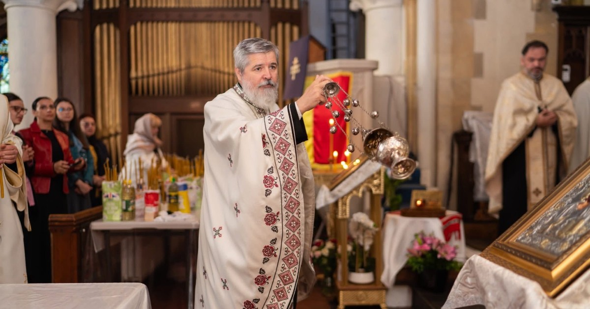 Un preot oficiază o slujbă religioasă într-o biserică, ținând în mână o cădelniță folosită în cadrul ritualurilor ortodoxe. În jurul său se află credincioși adunați la rugăciune, iar interiorul lăcașului de cult este decorat cu icoane și obiecte specifice tradiției creștine.