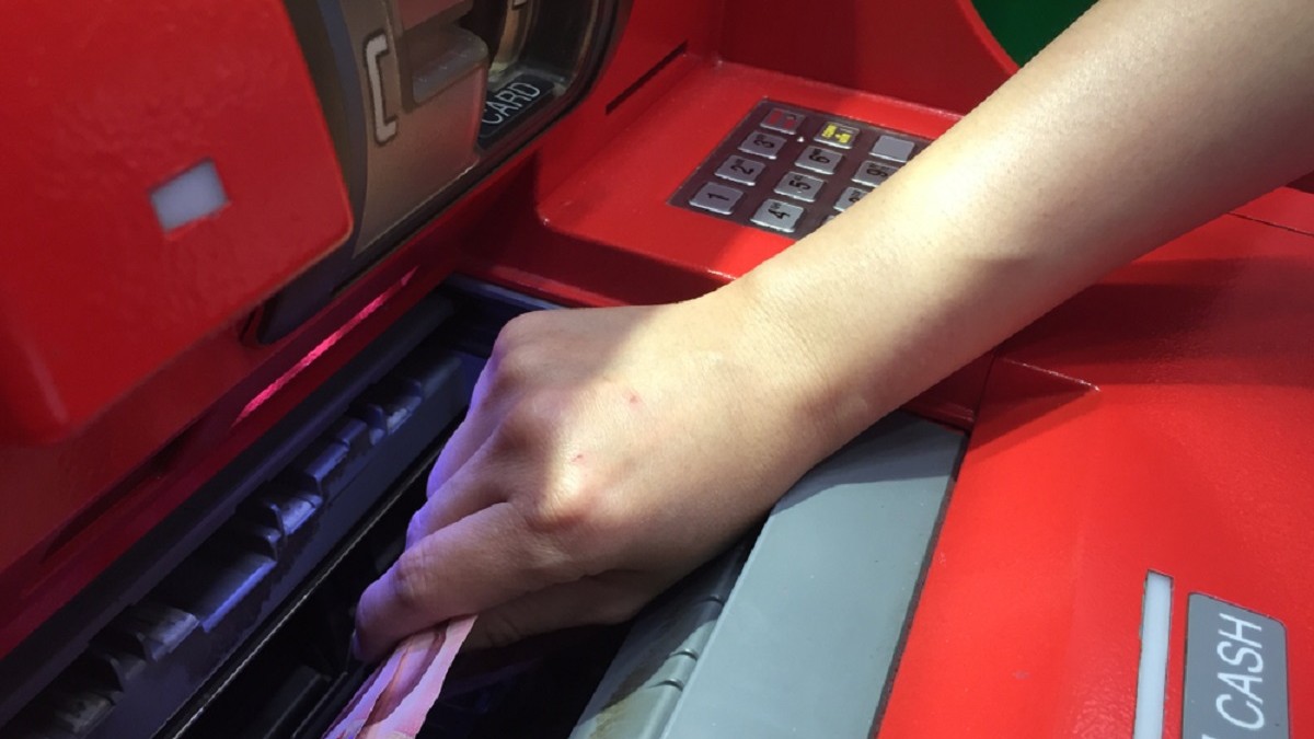 Cine poate retrage banii din contul unei persoane decedate - Imagine cu o mână de femeie care extrage bani dintr-un bancomat roşu.