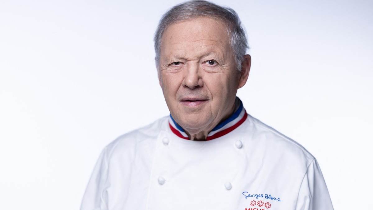 Georges Blanc, în vârstă de 82 de ani, bucătar șef. Poartă un un costum alb de bucătar pe care se vîăd brodate trei stele Mischelin