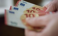 o mână care ține câteva bancnote de 10 euro, roșii și galbene