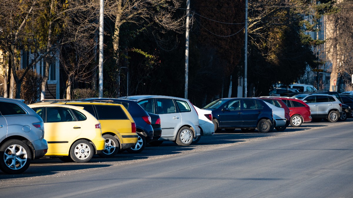 Imaginea prezintă un șir de mașini parcate pe marginea unui drum, pe o bandă de circulație. Majoritatea autovehiculelor sunt de tip hatchback, de culori diferite, printre care se remarcă un hatchback galben. Din cauza unghiului, nu se vede clar dacă mașinile sunt parcate legal.