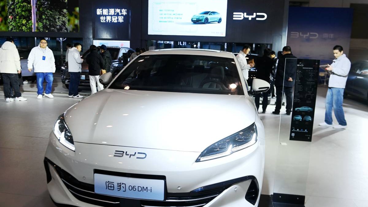 masina electrica alba prezentata intr-un showroom din china. in spatele ei sunt cateva persoane
