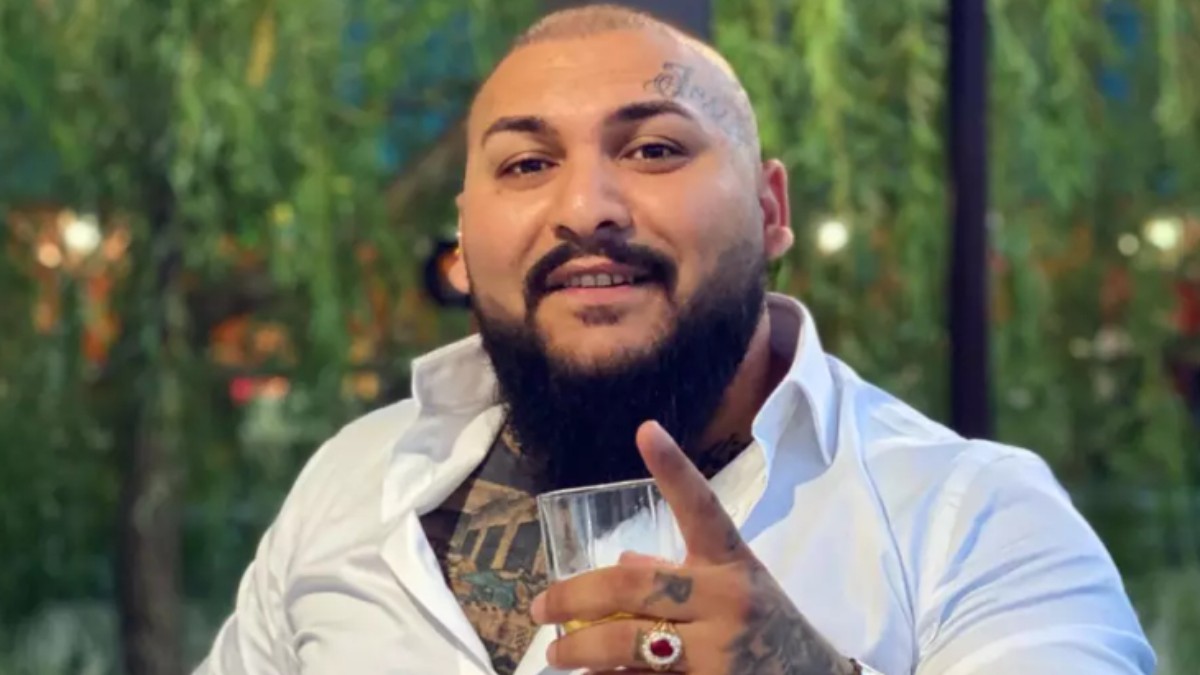 Dani Mocanu cu o cămașă albă și un pahar în mână.
