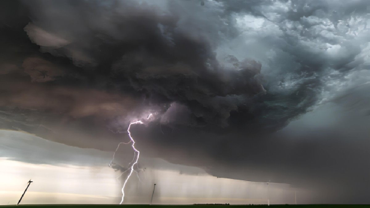 Imaginea surprinde un fenomen meteorologic extrem, înfățișând un fulger care lovește pământul sub o formațiune masivă de nori de furtună de tip supercelulă, deasupra unui câmp deschis.