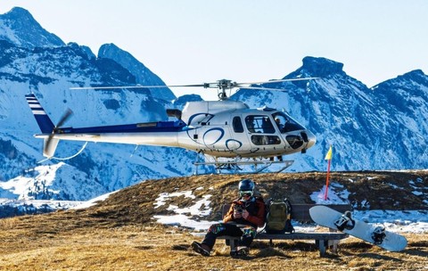 Un elicopter pe o platformă de aterizare de pe un munte înzăpezit, cu un peisaj alpin pitoresc în fundal
