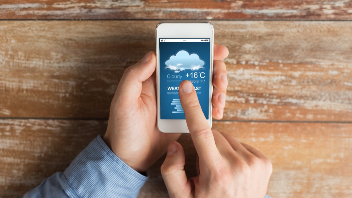 Un bărbat care apasă cu degetul pe ecranul telefonului, unde are o aplicație meteo deschisă