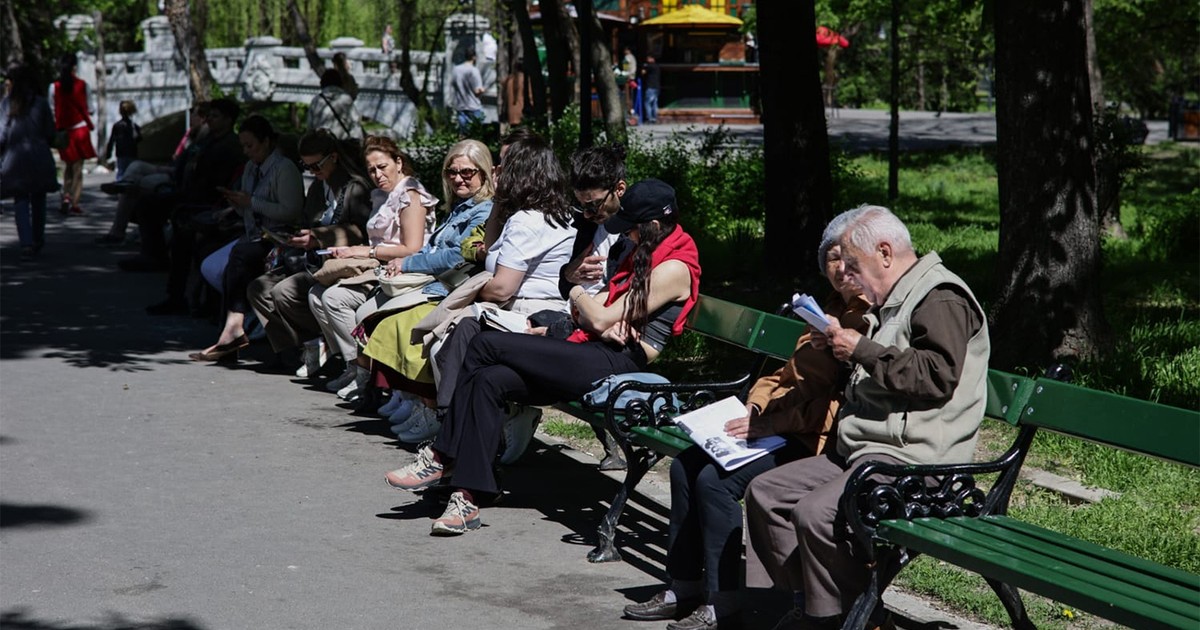 Mai mulți pensionari stau pe o bancă în parcul Cișmigiu din București