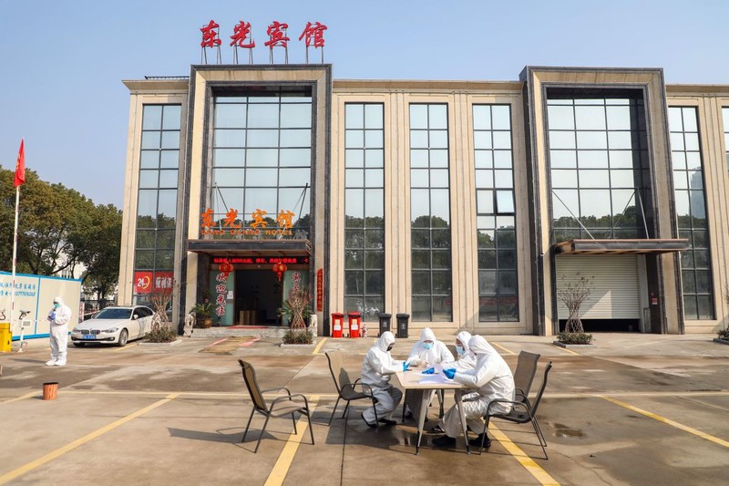 Câțiva oameni în costume de protecție discută la o masă în fața unui spital din Wuhan, China FOTO: EPA