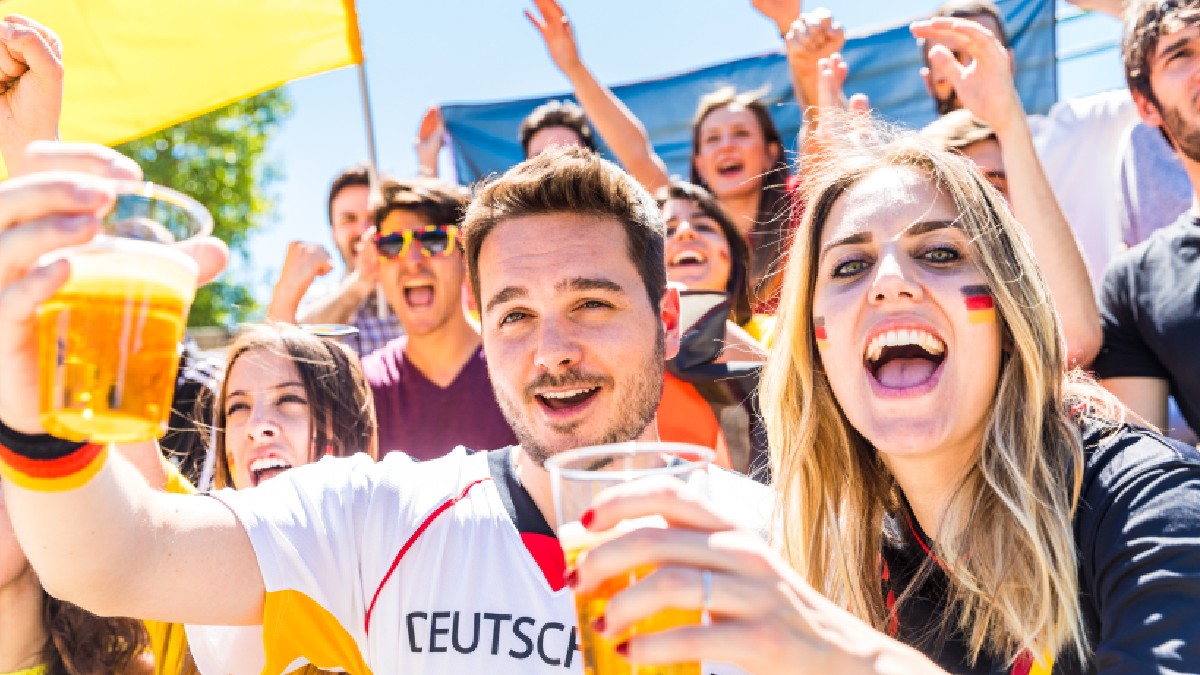 Fani germani care sărbătoresc pe stadion, consumând bere. Grup de suporteri urmărind un meci și susținând echipa națională a Germaniei. Tema combină sportul cu stilul de viață.