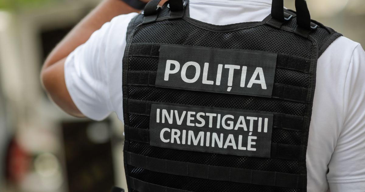 bărbat îmbrăcat într-o cămașă albă și o vestă neagră de poliție, cu textul „POLIȚIA INVESTIGAȚII CRIMINALE”, văzut de la spate