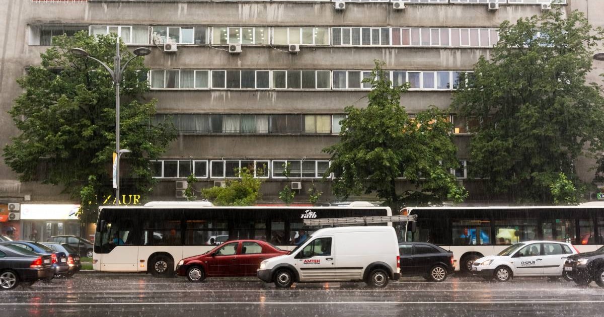 Mașini în București, stau la coadă la semafor într-o zi ploioasă, crengile copacilor se mișcă în bătaia vântului