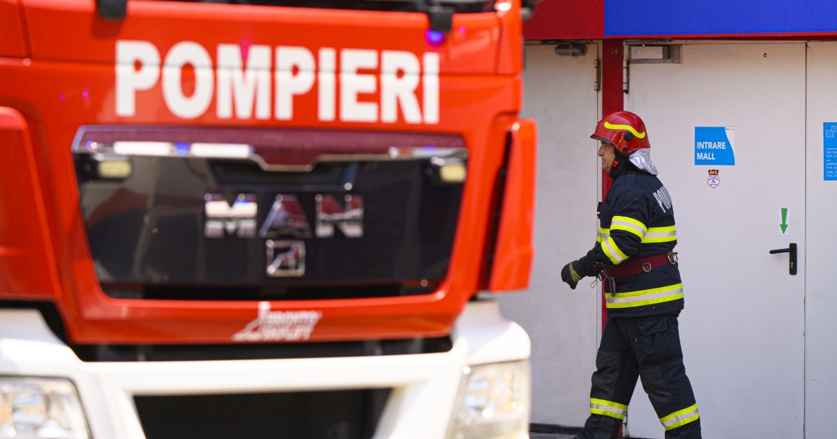 Un pompier echipat pentru intervenție intră într-o clădire, lângă o autospecială.