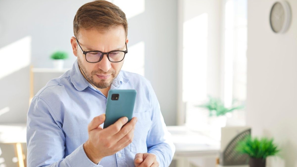 Un bărbat concentrat se uită pe ecranul telefonului mobil