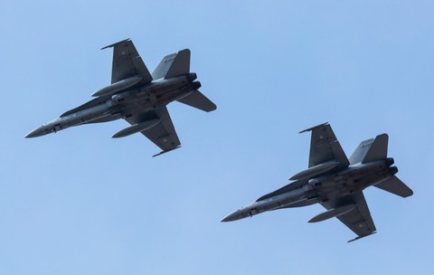 Imaginea prezintă două avioane militare de vânătoare F/A-18 Hornet zburând în formație